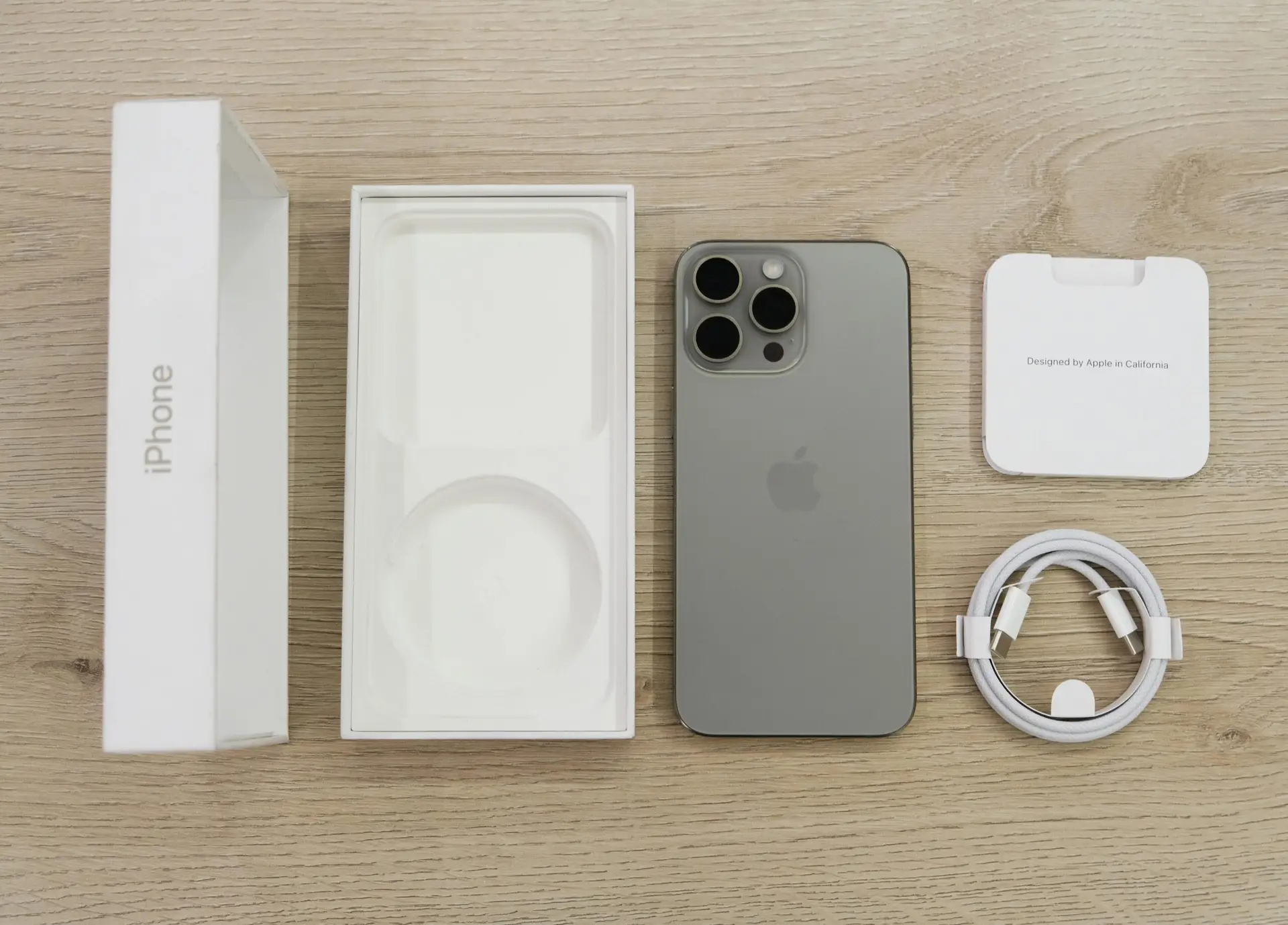 Flat lay view of the newest Apple iPhone model, box, and charging accessories on a wooden table.