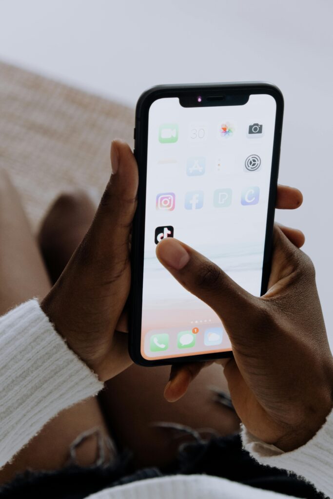 Hands holding a smartphone showing various apps including TikTok in a close-up view.