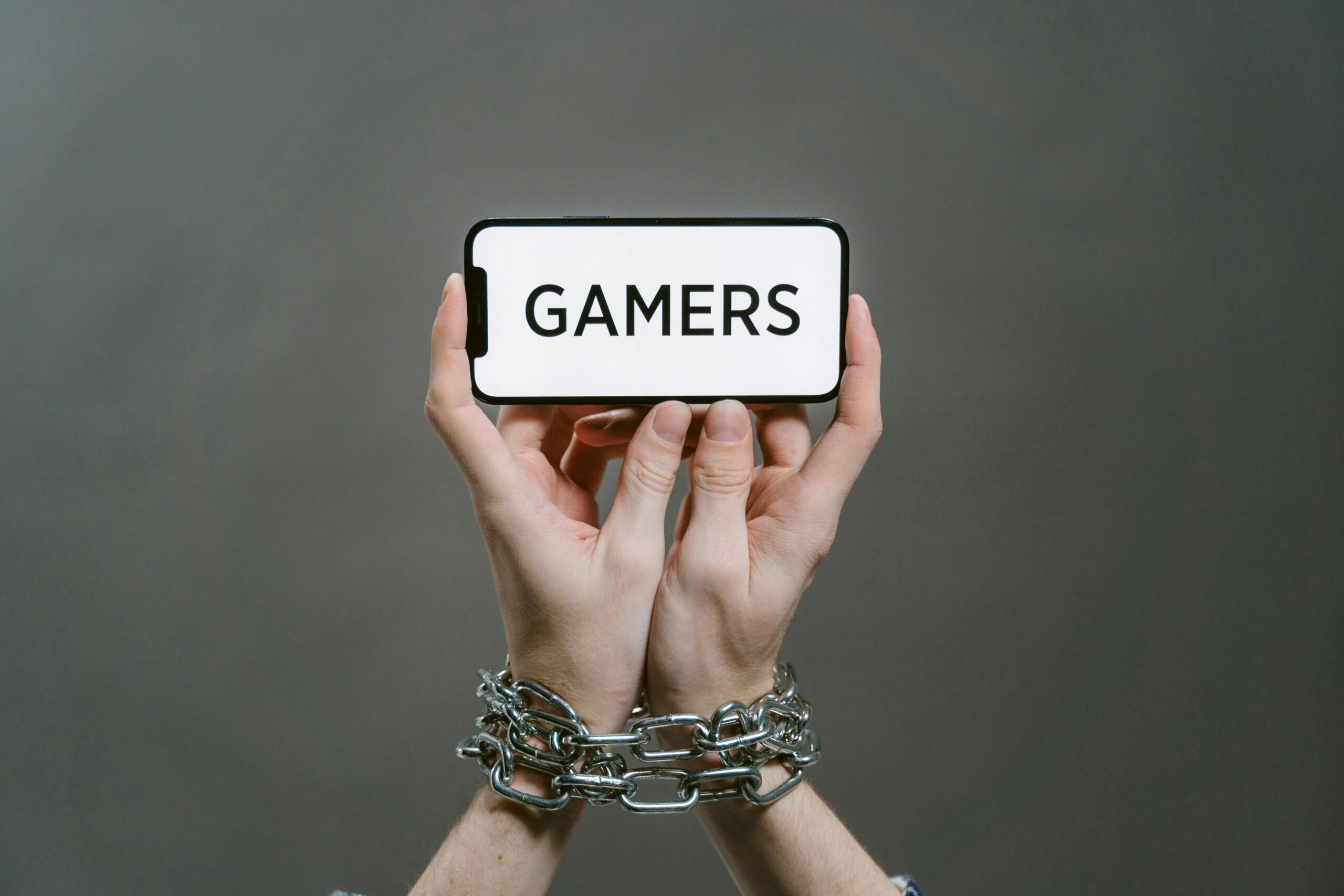 Conceptual image of a person holding a smartphone labeled 'GAMERS' with chained hands.