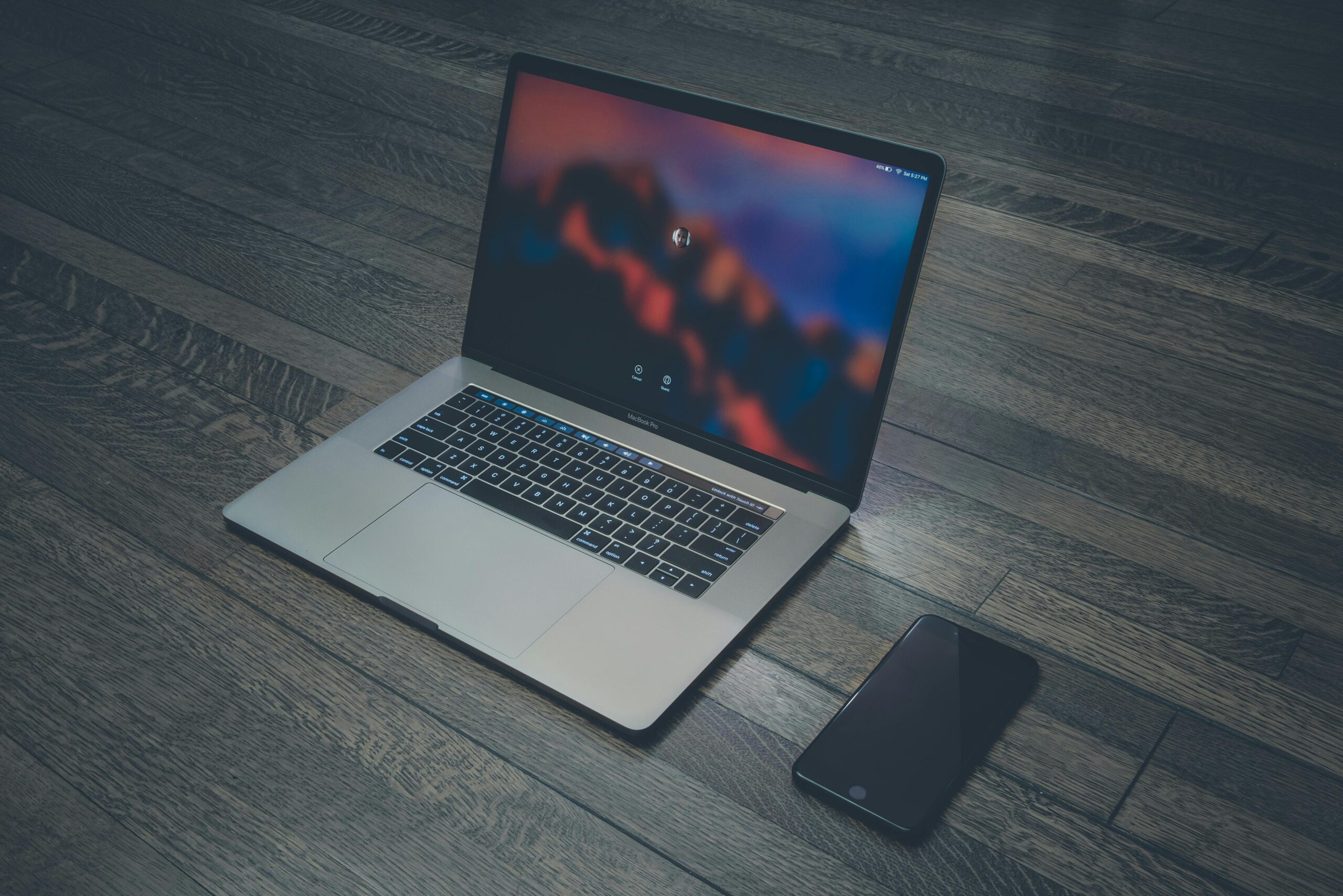 A sleek laptop and smartphone placed on wooden flooring, showcasing contemporary technology.