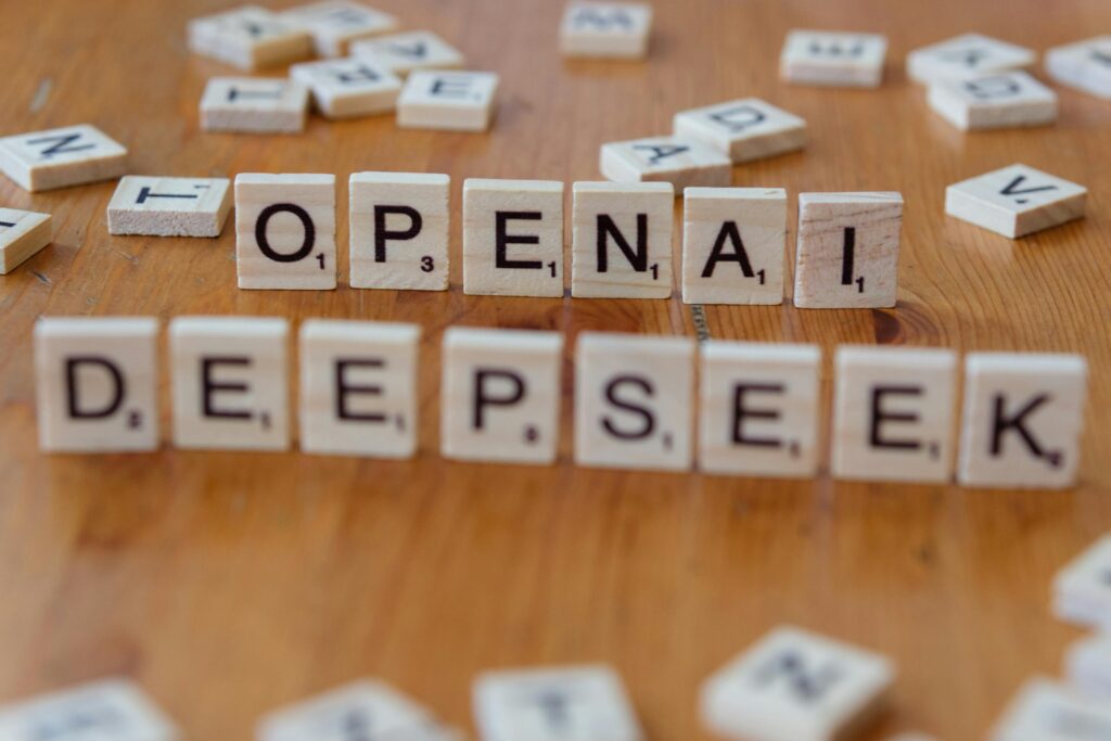 Close-up of wooden Scrabble tiles spelling OpenAI and DeepSeek on wooden table.